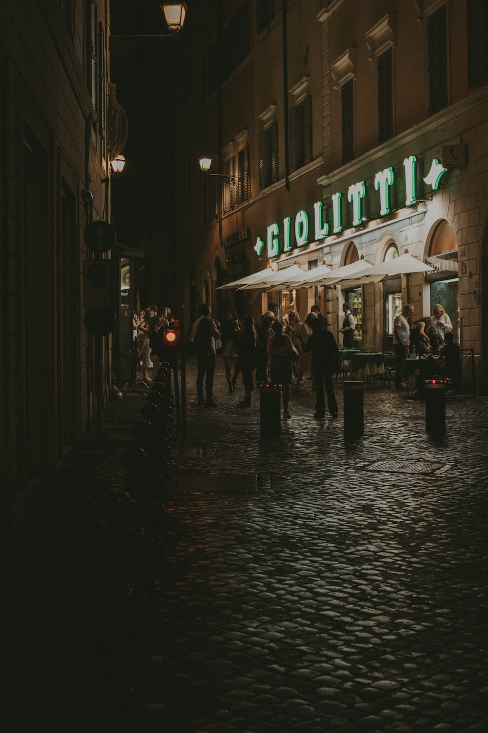 Persone socializzano fuori dal caffè illuminato Giolitti di notte.