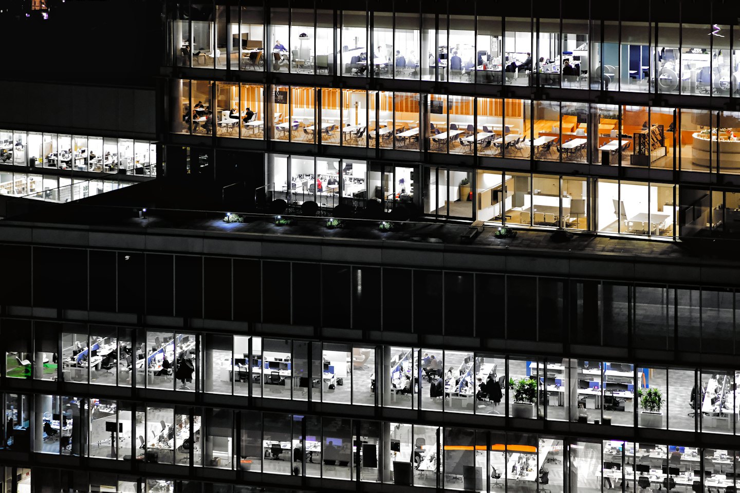 Moderno edificio per uffici illuminato di notte con impiegati al lavoro all'interno.