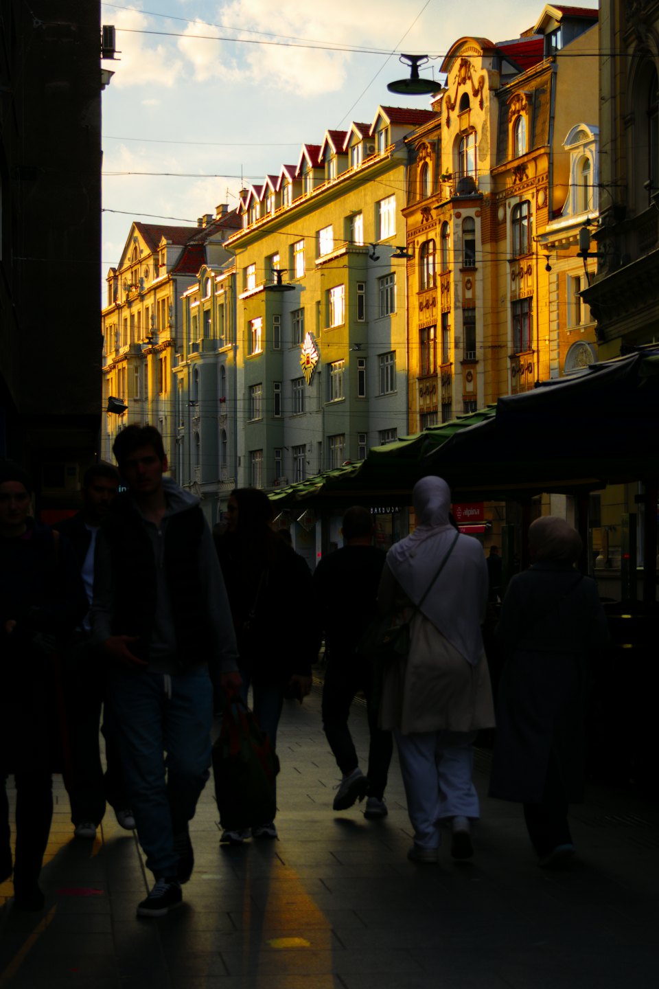 Pedoni passeggiano lungo una strada cittadina fiancheggiata da edifici ornati.
