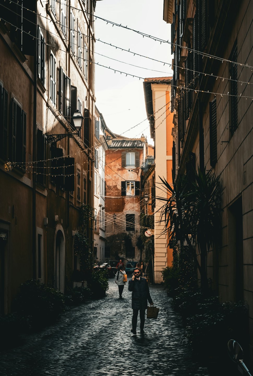 Un uomo parla al telefono mentre cammina per una strada acciottolata.